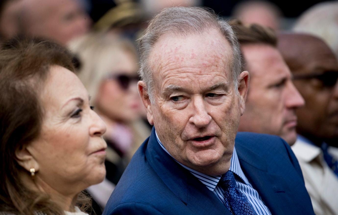 Bill O’Reilly, in a blue suit and blue striped shirt, talks to a woman.