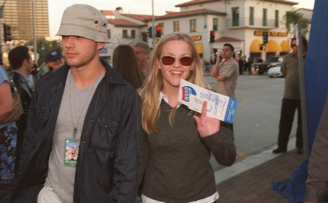 Ryan Phillippe, in a grey tshirt, hat, and black coat, walks alongside Reese Witherspoon who wears a grey sweater over a white shirt.