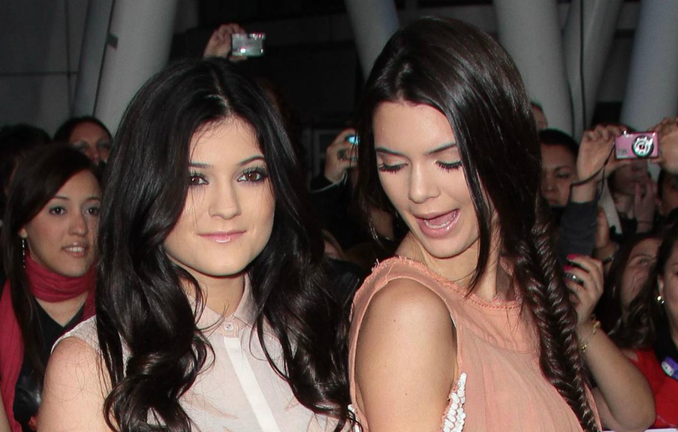 Kylie Jenner, in an off-white blouse, poses on the red carpet alongside sister Kendall who wears a peach-colored dress.