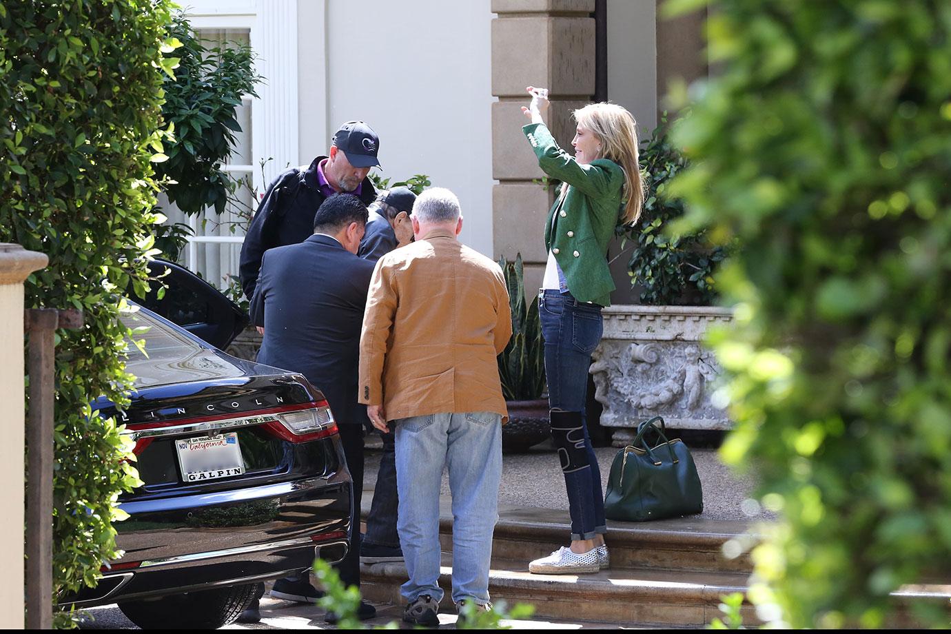 Larry King Wearing Baseball Cap Being Helped Out Of Car While Shawn Wearing a Green Jacket And Jeans Takes Photos of Trees With Phone