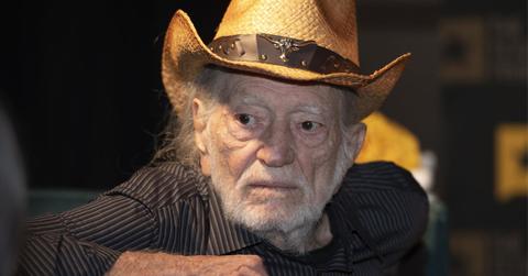 Willie Nelson Looking Left Wearing Straw Cowboy Hat and Brown Striped Shirt