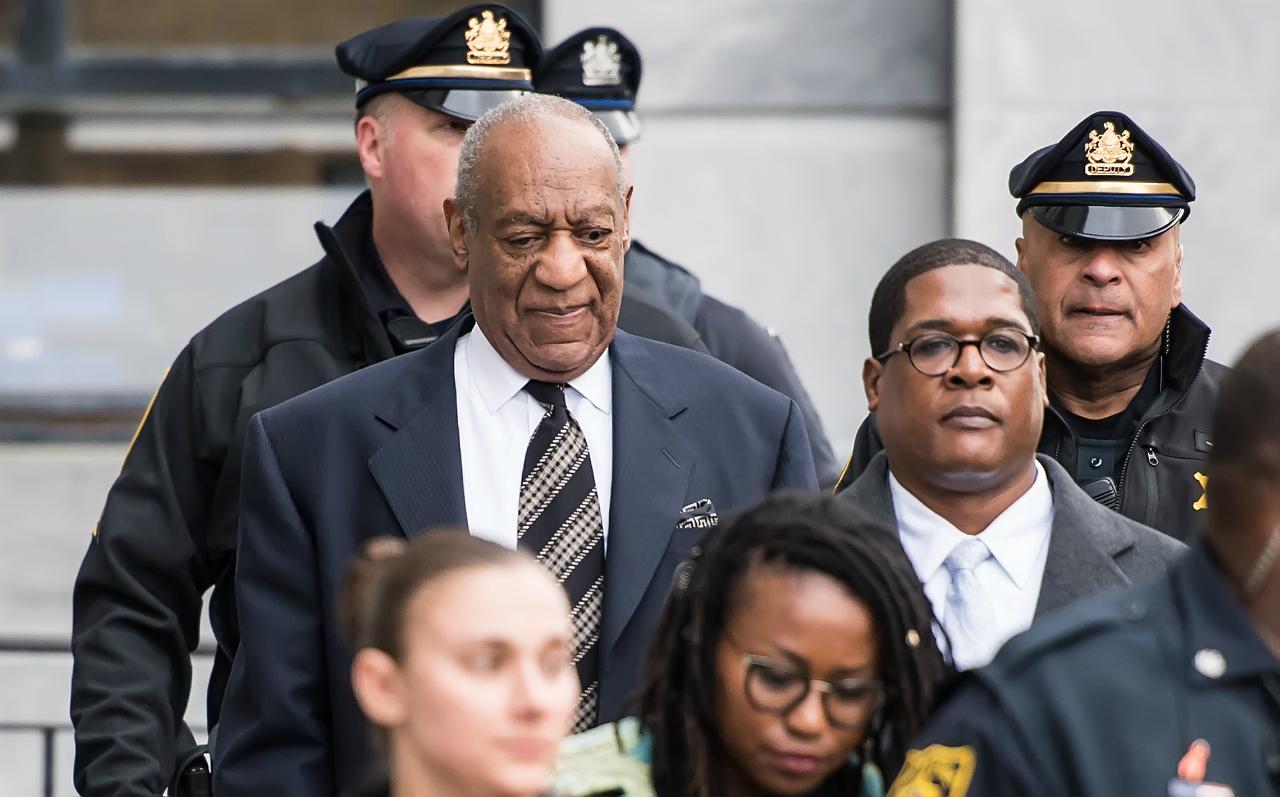 Bill Cosby walks out of court in front of police officers, next to his lawyer.