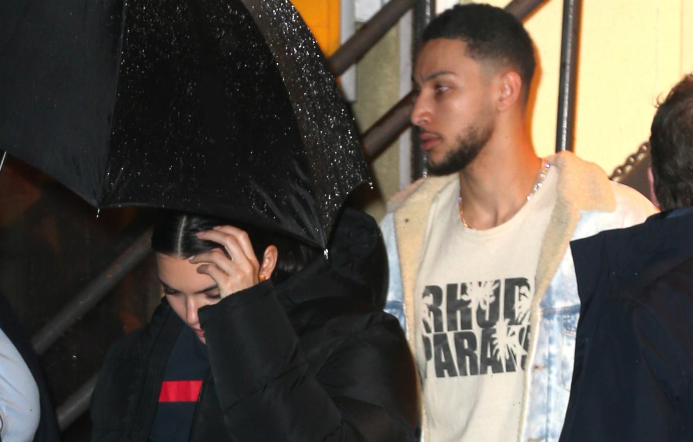 Kendall Jenner, in black, covers her face as Ben Simmons, in white, walks behind her.