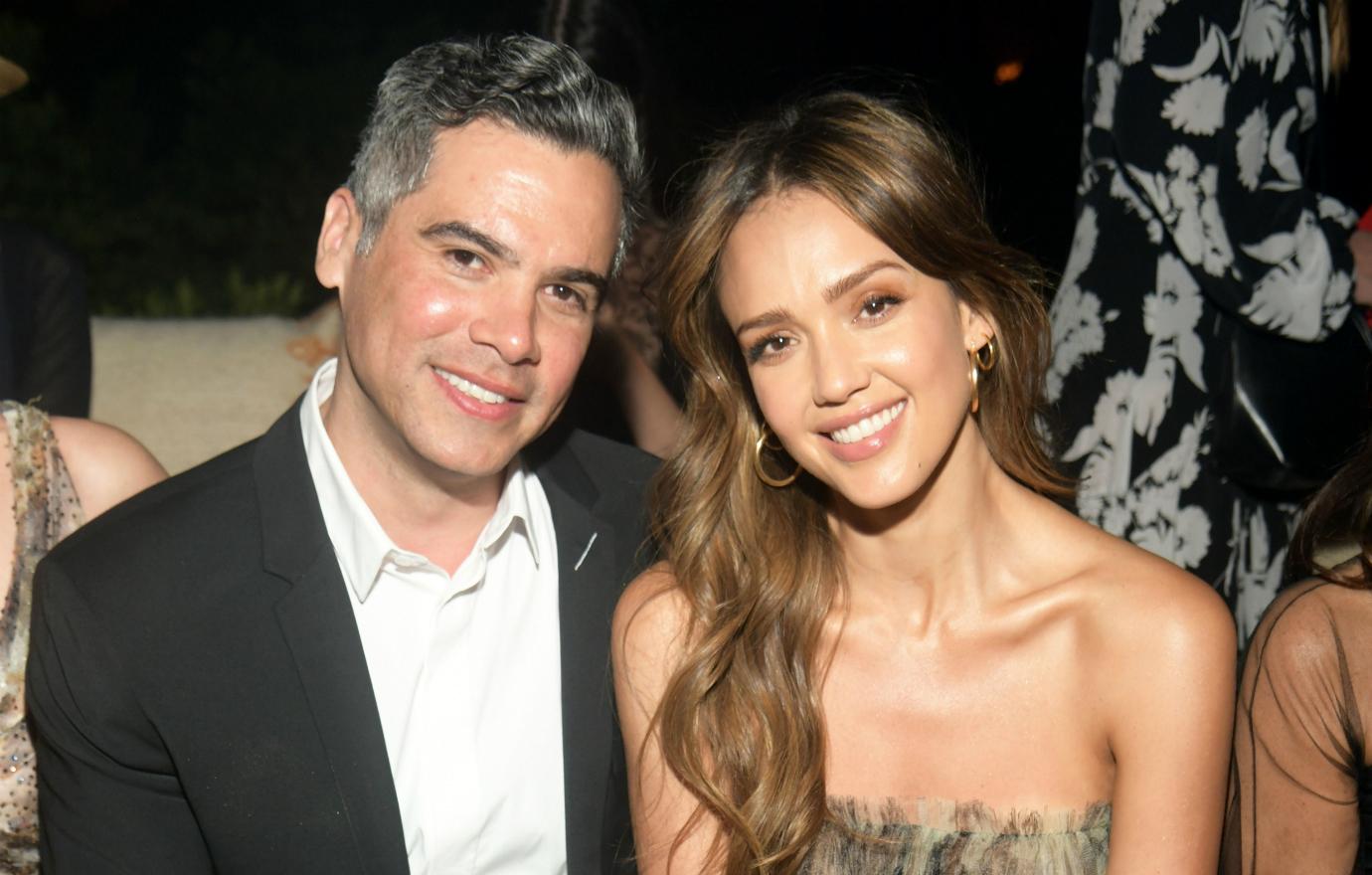 Cash Warren, in a black suit and white tie, sits next to Jessica Alba who wears a flowy dress.