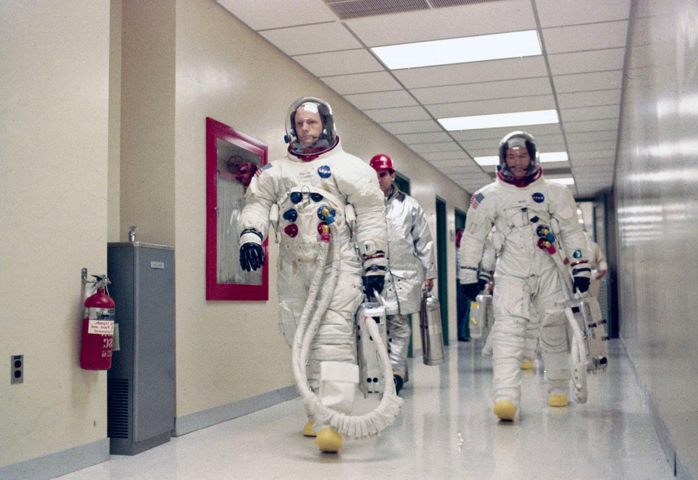 Apollo 11 Commander Neil Armstrong leading Michael Collins and Edwin Buzz Aldrin (hidden behind Collins) down a corridor on their way to participate in the launch countdown demonstration test.